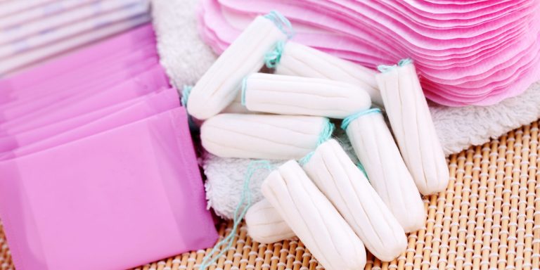 Tampons and sanitary pads are arranged on a textured surface.